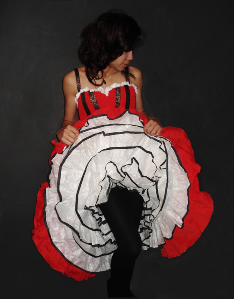 May include: A woman wearing a red and white dress with black trim. The dress has a large, ruffled skirt.