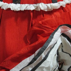 May include: A red, crinkled paper skirt with a white ruffle trim and black and white striped trim.