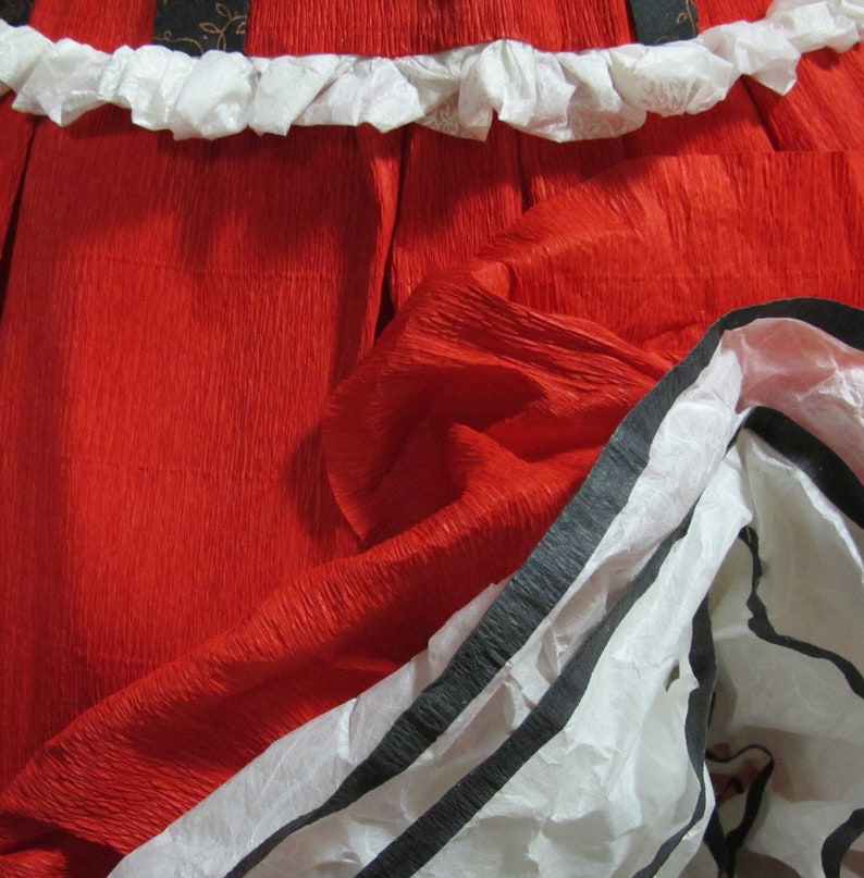 May include: A red, crinkled paper skirt with a white ruffle trim and black and white striped trim.