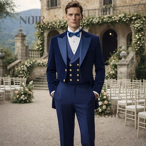 May include: A formal navy blue tuxedo with a velvet jacket, vest, and trousers. The jacket has a contrasting satin lapel and gold buttons. A white dress shirt and blue bow tie complete the ensemble. The word "NOIR" is visible in the upper left corner.