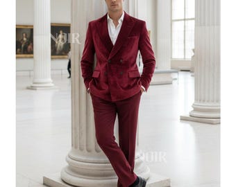 May include: A burgundy velvet suit with a double-breasted jacket and matching trousers. The suit is paired with a white dress shirt and black dress shoes. The man is leaning against a white column in a museum setting.
