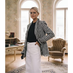 Puede incluir: Una blazer de pata de gallo en blanco y negro con bordes deshilachados. La blazer se lleva sobre una camiseta negra y unos vaqueros blancos. La palabra "NOIR" es visible en la imagen.