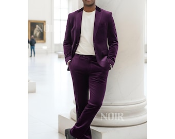 May include: A deep purple velvet suit, including a blazer and trousers, paired with a white crew neck shirt. The suit is worn with black leather dress shoes. The image is taken in a museum setting.