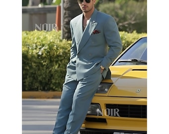 May include: A light blue double-breasted suit with matching trousers. The suit is worn with white sneakers and a red pocket square. The person is leaning against a yellow car. The word "NOIR" is visible on the car.