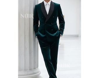 May include: A dark green velvet suit with a black lapel, double-breasted jacket, and matching trousers. The suit is paired with a white dress shirt. The word "NOIR" is visible on the pillar.