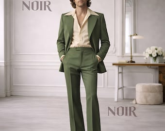 May include: A man in a green suit with a cream-colored shirt. The suit has a wide lapel and flared pants. The word "NOIR" is displayed in a stylized font. The man is wearing sunglasses and brown shoes. The background is a room with white walls and a mirror.