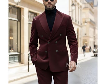 May include: A burgundy double-breasted suit with a black turtleneck. The suit has a velvet texture and features dark buttons. The image is taken outdoors, with a blurred background of a city street.