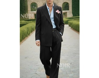 May include: A dark gray pinstripe suit with a light blue shirt and a pink flower in the lapel. The double-breasted suit has wide-leg pants and a black belt. The word "NOIR" is visible in the image.