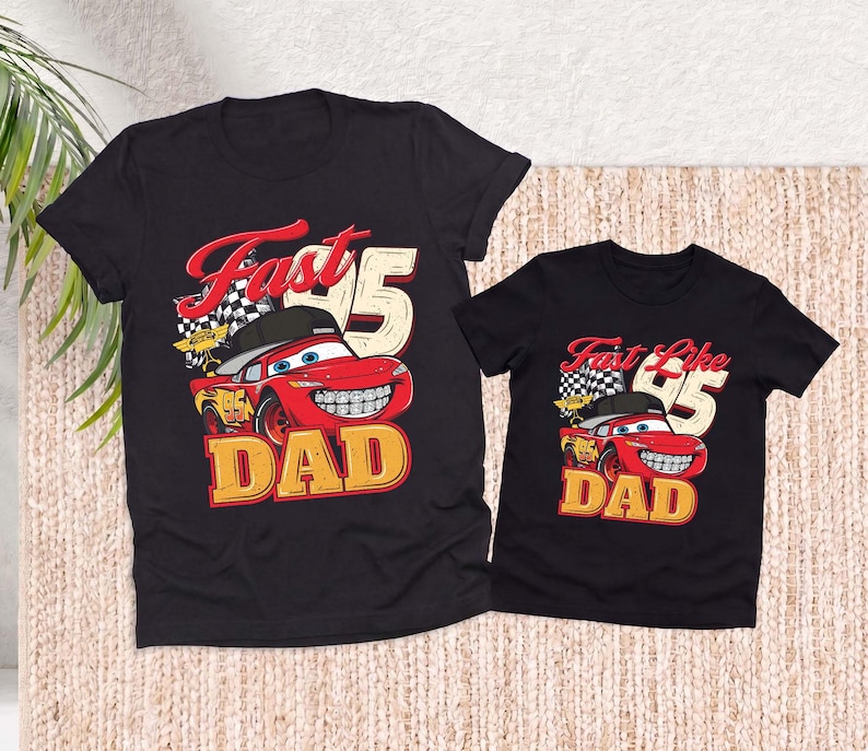 May include: Two black short-sleeve t-shirts featuring a graphic of a red race car wearing a black baseball cap and braces. The design includes a checkered flag, the number 95, and the text Fast DAD on the larger shirt and Fast Like DAD on the smaller.
