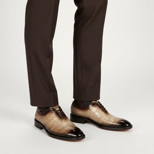 May include: Brown leather dress shoes with a crocodile skin pattern. The shoes have a dark brown toe and a black sole. The shoes are laced up and are worn with brown dress pants.