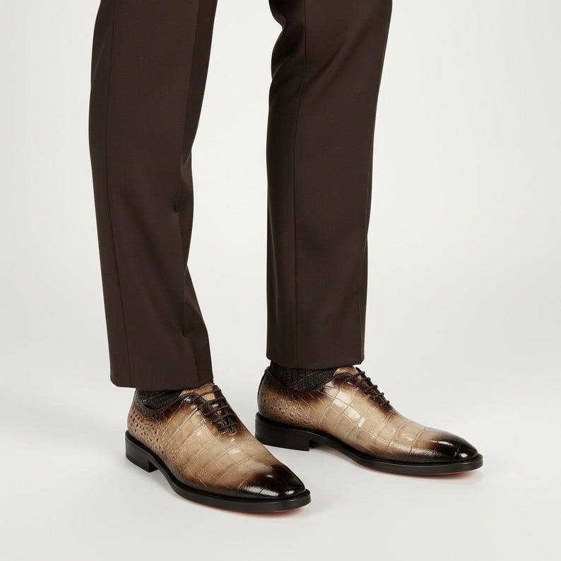 May include: Brown leather dress shoes with a crocodile skin pattern. The shoes have a dark brown toe and a black sole. The shoes are laced up and are worn with brown dress pants.