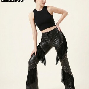 May include: Black leather trousers with fringe and stud detailing. The trousers feature a lace-up front and are worn with a black ribbed crop top. The text "LEATHERLEAVESCO." is visible in the upper left corner.