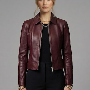 May include: A burgundy leather jacket with a zip-up front, collared neckline, and long sleeves. The jacket is paired with black pants and a black top. The image includes the text "LEATHER LEAVES PVT LTD".