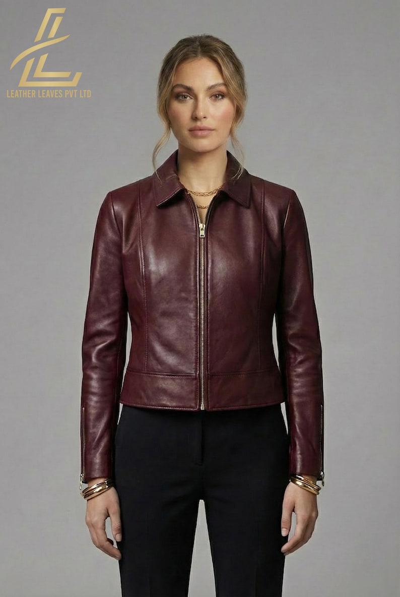 May include: A burgundy leather jacket with a zip-up front and a collared neckline. The jacket is paired with black pants. The image also shows the text "LEATHER LEAVES PVT LTD" in the upper left corner.