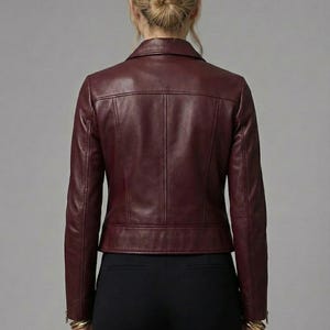 May include: Burgundy leather jacket with a classic collar and a tailored fit. The jacket features a front zipper closure and a subtle, textured finish. The back view showcases the jacket's design and stitching details. The brand logo is visible in the upper left corner.