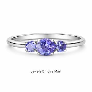 Könnte beinhalten: Ein silberner Ring mit drei hellvioletten Edelsteinen. Der zentrale Stein ist größer als die beiden seitlichen Steine. Der Ring ist vor einem weißen Hintergrund platziert, darunter der Text "Jewels Empire Mart".