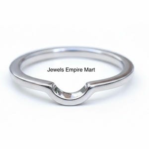 May include: A silver-colored ring with a curved design. The ring has a smooth, polished surface and a slight arch in the center. The text "Jewels Empire Mart" is visible on the ring.