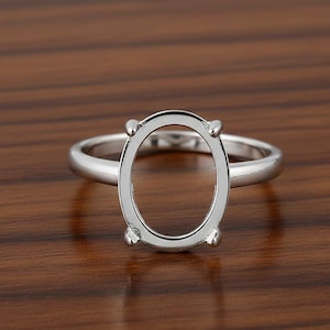 Könnte beinhalten: Ein silberfarbener Ring mit ovaler Fassung, zur Aufnahme eines Edelsteins. Der Ring ist vor einem dunklen Holzmaserungshintergrund platziert, der seine polierte Metalloberfläche hervorhebt. Das Design des Rings weist vier Krappen zur Sicherung des Steins auf.