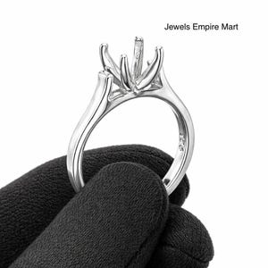Könnte beinhalten: Eine silberne Ringfassung mit Zinken zur Aufnahme eines Edelsteins. Der Ring wird von einer behandschuhten Hand gehalten. Der Text "Jewels Empire Mart" ist oben rechts sichtbar.