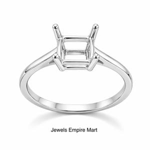 Könnte beinhalten: Eine silberne Verlobungsringfassung mit quadratischer Mitte und vier Krappen. Der Ringband ist glatt und poliert. Der Text "Jewels Empire Mart" befindet sich am unteren Rand des Bildes.