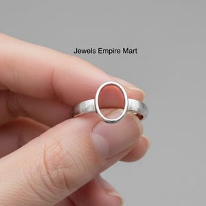 Könnte beinhalten: Ein silberner Ring mit einer ovalen Fassung. Der Ring wird in einer Hand gehalten. Der Text "Jewels Empire Mart" ist im Bild zu sehen.