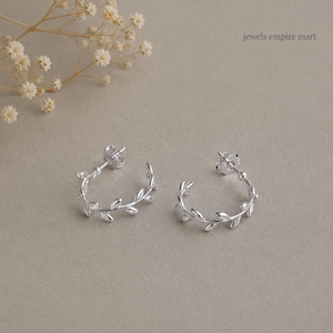 May include: A pair of silver hoop earrings featuring a delicate leaf vine design. Each earring is a semi-circular hoop with small, polished silver leaves attached along the outer edge. The earrings include standard post backs and the text jewels empire mart.