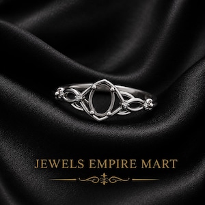 May include: A silver-toned metal ring featuring an empty oval-shaped central setting flanked by intricate, interwoven metal loops and small, clear, round-cut stones. The text JEWELS EMPIRE MART is displayed below the ring with a decorative line element.