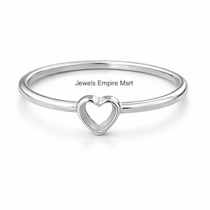 Könnte beinhalten: Ein silberner Ring mit herzförmigem Design. Der Ring hat ein zartes Band und ein hohles Herz in der Mitte. Der Text "Jewels Empire Mart" ist auf dem Bild sichtbar.