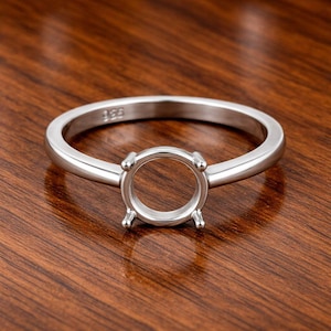 Könnte beinhalten: Ein silberner Ringrohling mit runder Lünette und vier Krappen. Der Ring liegt auf einer Holzoberfläche. Der Ring ist mit der Zahl 925 markiert.