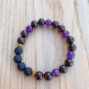 May include: A purple and black beaded bracelet with gold accents. The bracelet is made with amethyst and garnet beads, and lava rock beads.