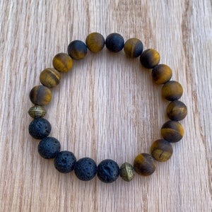 May include: A bracelet made of tiger's eye and lava rock beads with gold accents. The bracelet has a brown and black color scheme.