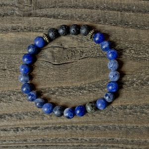 May include: A blue and black beaded bracelet with gold accents. The bracelet is made with round beads and is on a wooden surface.