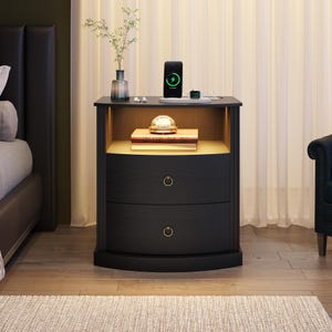 May include: A black wooden nightstand featuring two curved drawers with circular metal pulls, an open storage shelf with integrated warm lighting, and a flat top surface holding a smartphone, a smartwatch, and a glass vase with greenery.
