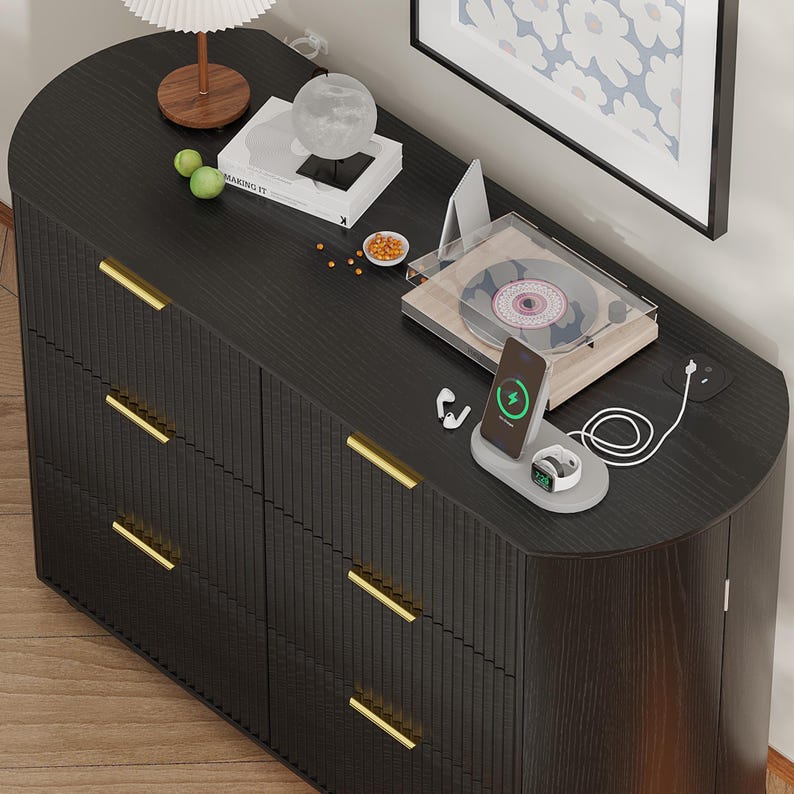 May include: A dark wood dresser with gold handles, topped with a lamp, books, and decorative items. A record player, charging station, and framed artwork are also on display, creating a stylish and functional storage solution.