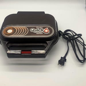 May include: A black and brown Oster Quick 6 Donut Baker. The appliance has a red switch and a brown and white graphic of donuts. The power cord is black.