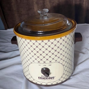 May include: A Crock-Pot stoneware slow cooker with a glass lid. The slow cooker has a cream-colored body with a geometric pattern and brown accents. It features a dial with settings for off, low, and high.