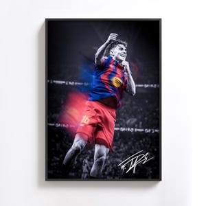 May include: A framed print featuring a soccer player in a red and blue jersey, number 16, celebrating a goal. The background is a blurred stadium scene, with the player's signature in the lower right corner. The image is in color with a black and white background.