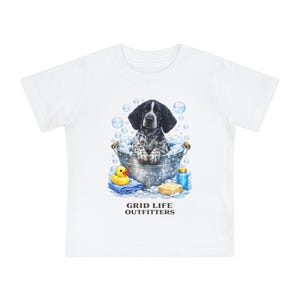 Op de afbeelding: Wit T-shirt met een aquarel illustratie van een hond in een metalen badkuip vol bellen. Een gele badeend, zeep en een blauwe fles staan ook op de afbeelding. De tekst "GRID LIFE OUTFITTERS" staat onderaan.