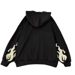 May include: Black hoodie with a hood and long sleeves. The sleeves feature a flame design in a lighter color. The hoodie is made of a soft material and is suitable for casual wear.