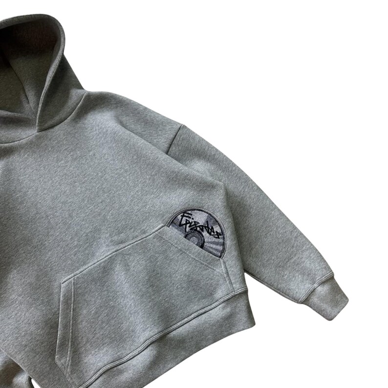 Puede incluir: Una sudadera con capucha gris con bolsillo de canguro y capucha. La manga izquierda tiene un parche circular con la palabra "Episodes" y un dise&ntilde;o de CD. La sudadera est&aacute; hecha de un material suave.