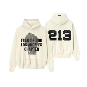 May include: Cream-colored hoodie with the text "FEAR OF GOD LOS ANGELES CHAPTER" on the front and the number "213" on the back. The text and numbers are in black, distressed font. The hoodie has a hood and long sleeves.