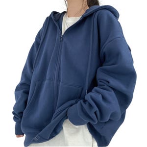 May include: A navy blue zip-up hoodie with a hood and front pockets. The hoodie is made of a soft material and has a relaxed fit. The zipper runs down the center of the hoodie.