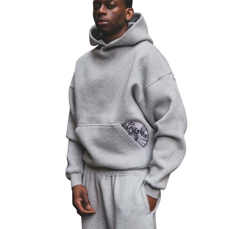 Puede incluir: Un conjunto de sudadera con capucha y pantal&oacute;n de ch&aacute;ndal grises. La sudadera con capucha tiene un bolsillo de canguro con un dise&ntilde;o bordado circular. El conjunto est&aacute; hecho de un material suave y c&oacute;modo.
