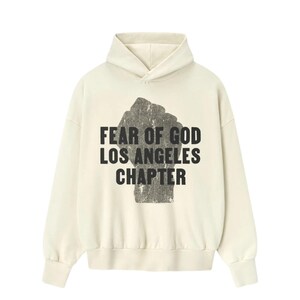 May include: Cream-colored hoodie with a black graphic of a clenched fist and the text "FEAR OF GOD LOS ANGELES CHAPTER" in a bold, sans-serif font. The hoodie features a drawstring hood and long sleeves.