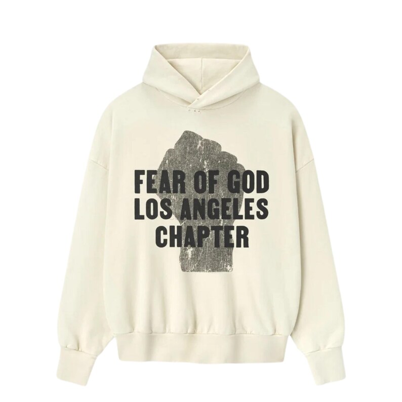 May include: Cream-colored hoodie with a black graphic of a clenched fist and the text "FEAR OF GOD LOS ANGELES CHAPTER" in a bold, sans-serif font. The hoodie features a drawstring hood and long sleeves.