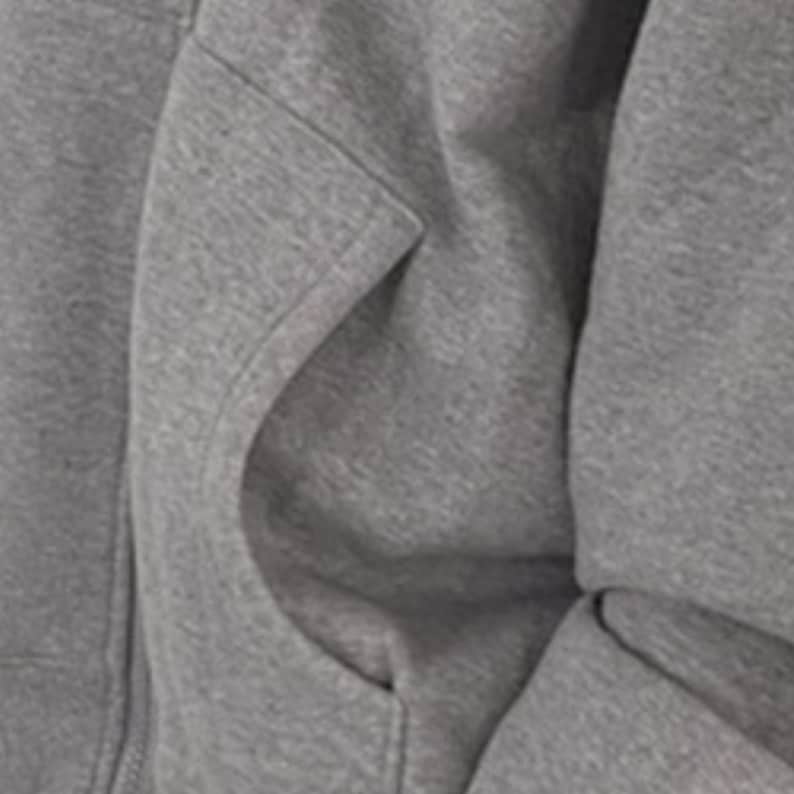 May include: Close-up of a gray hoodie with a kangaroo pocket. The fabric is a soft, textured material. The pocket is large and has a curved opening. The hoodie appears to be made of a thick, warm fabric, suitable for cooler weather.
