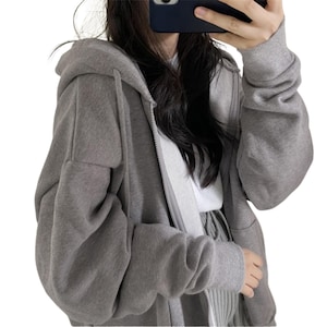 May include: A gray zip-up hoodie with a hood and long sleeves. The hoodie is made of a soft material and has a relaxed fit. The zipper runs down the front of the hoodie.
