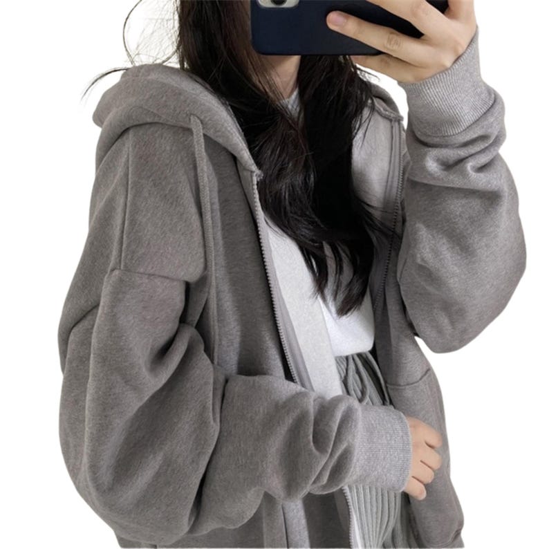May include: A gray zip-up hoodie with a hood and long sleeves. The hoodie is made of a soft material and has a relaxed fit. The zipper runs down the front of the hoodie.