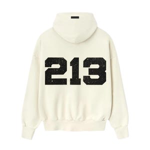 May include: Cream-colored hoodie with the number "213" printed in distressed black on the back. The hoodie features a hood and long sleeves. A small black rectangular detail is on the hood.