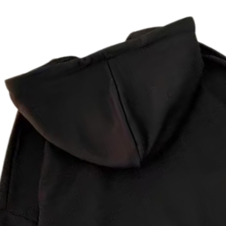 May include: A close-up of a black hooded sweatshirt. The hood is the primary focus, showcasing its shape and the fabric's texture. The image highlights the design and construction of the garment, emphasizing its dark color and casual style.